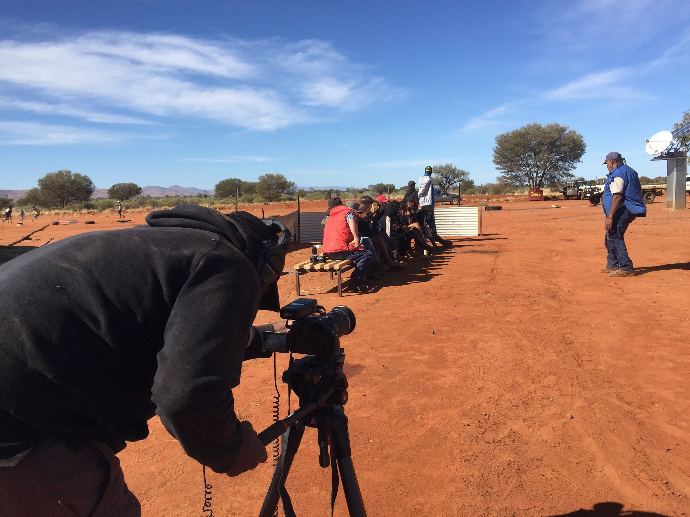 A video camera on a tripod on red earth, with the ranges behind