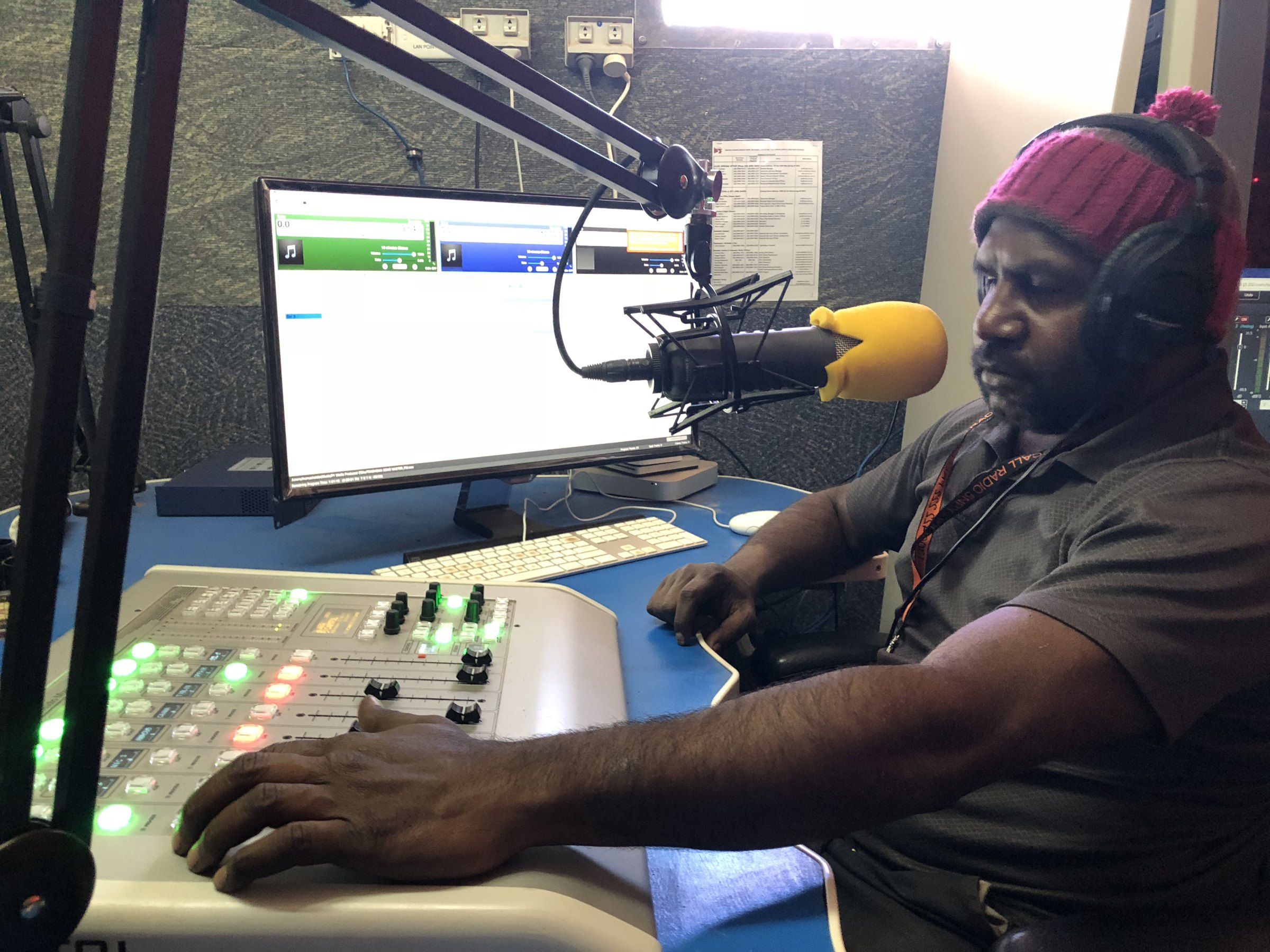 A broadcaster at the 5NPY studio desk in Umuwa, headphones on, in front of the mixing panel